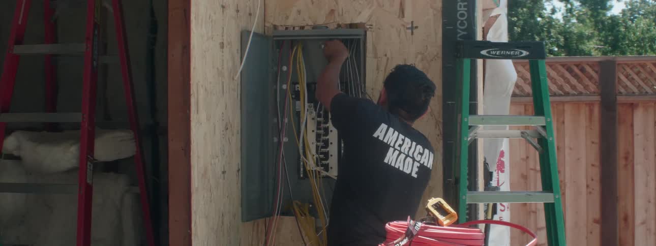 An electrician works with wires on a new electrical box on new home construction