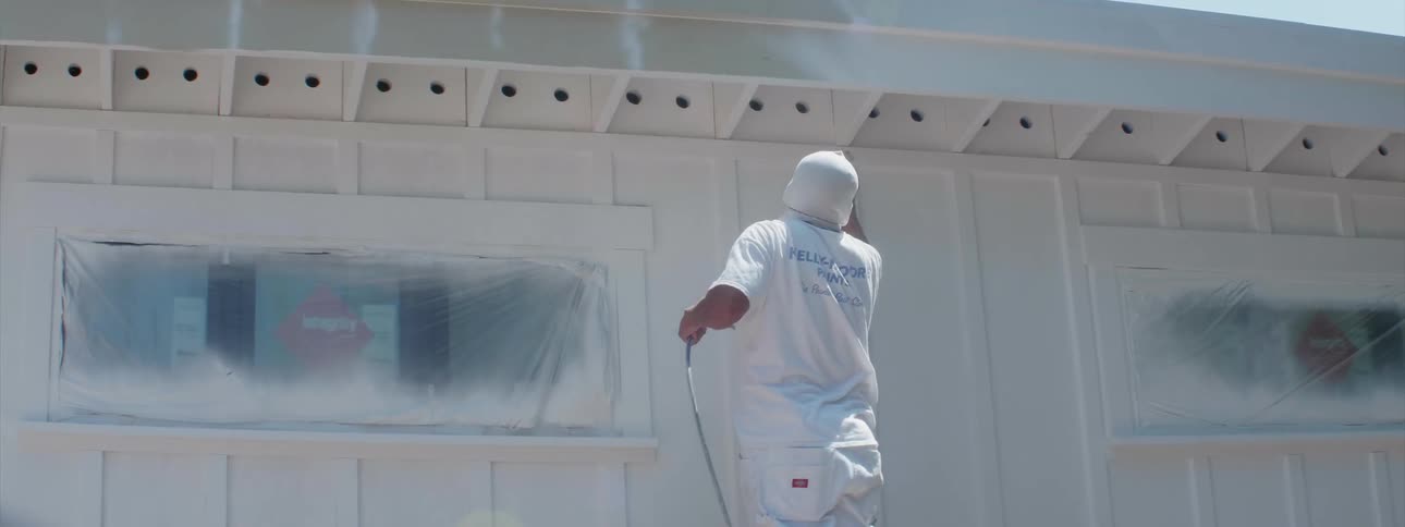 Man paints the side of a building with a spray gun