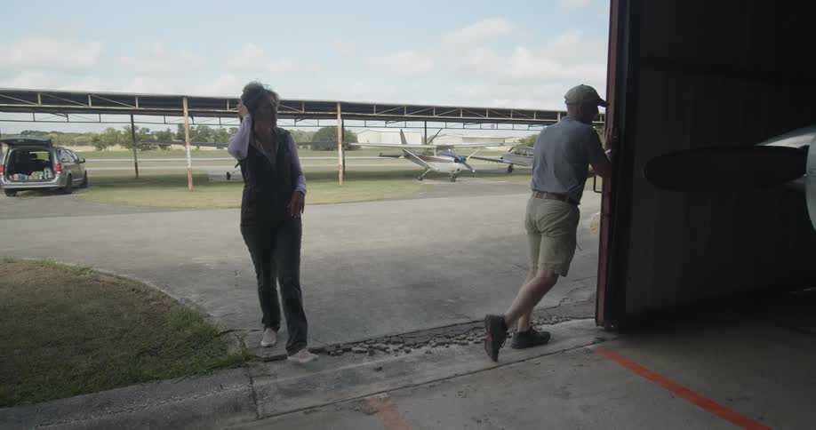 A man opens the sliding door of an airport hangar and a woman enters