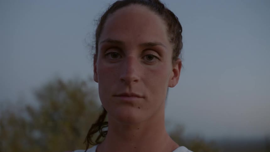 A woman with hair pulled back in a ponytail stands outside with the wind blowing