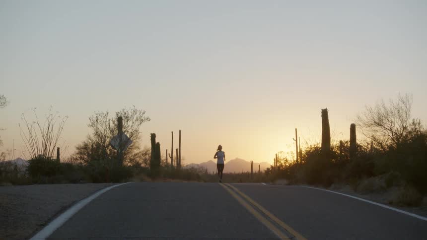 Woman jogging on a remote road through desert at sunrise