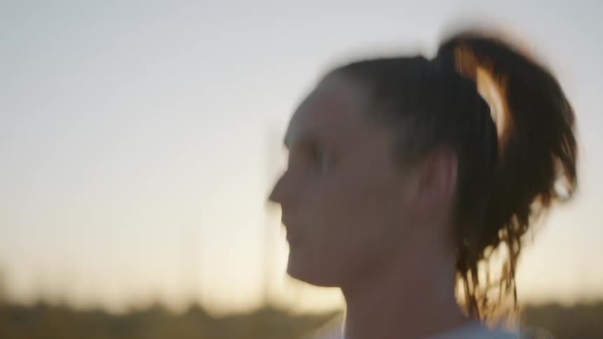 Woman with ponytail runs along the road at sunset