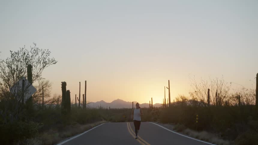 A woman jogging down the center of a road in the desert