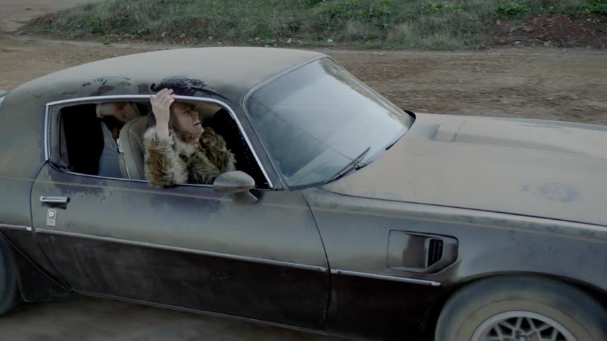 People laugh while riding in a dirt covered muscle car