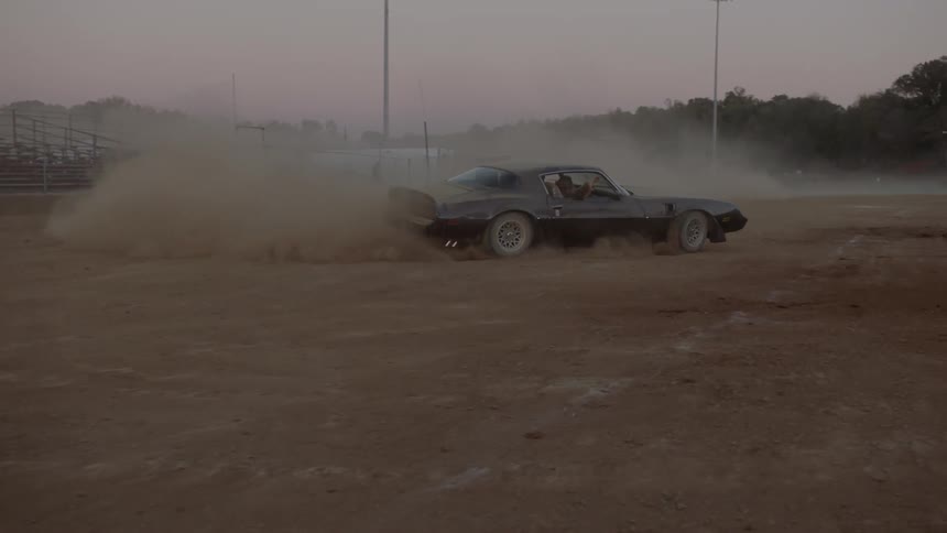A man drives his car fast in a dirt arena