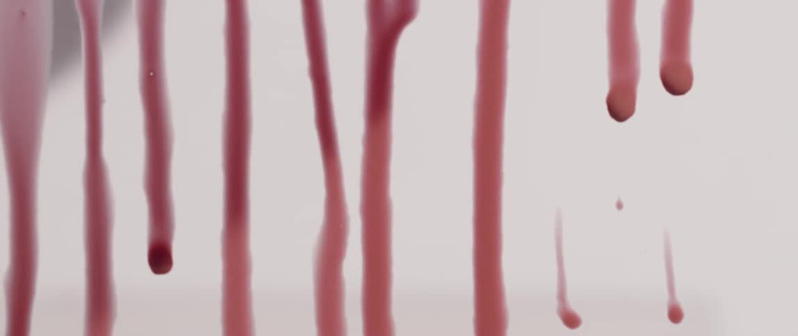 Viscous red liquid drips down a window as a shadow passes in the background