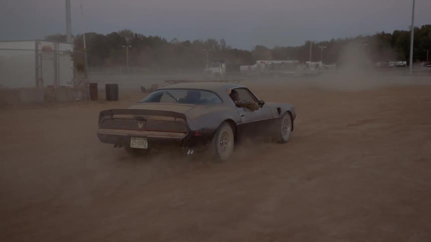 A car is driving in a rural area on a dirt road