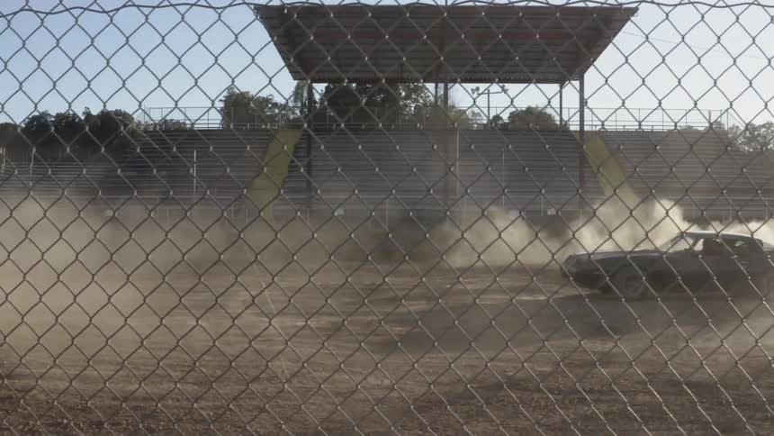 A car makes a fast turn in a dirt arena kicking up dust