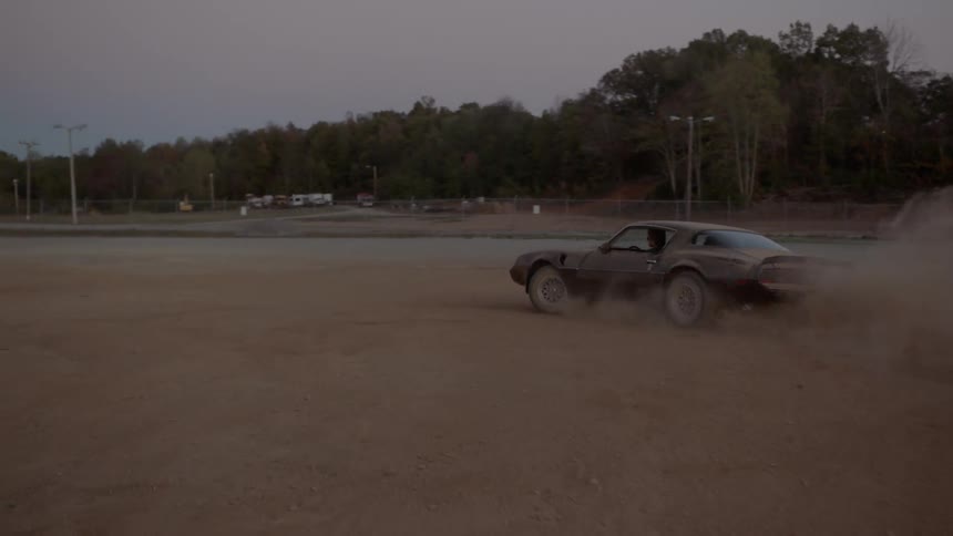 A man in a sports car spins out in a dirt lot