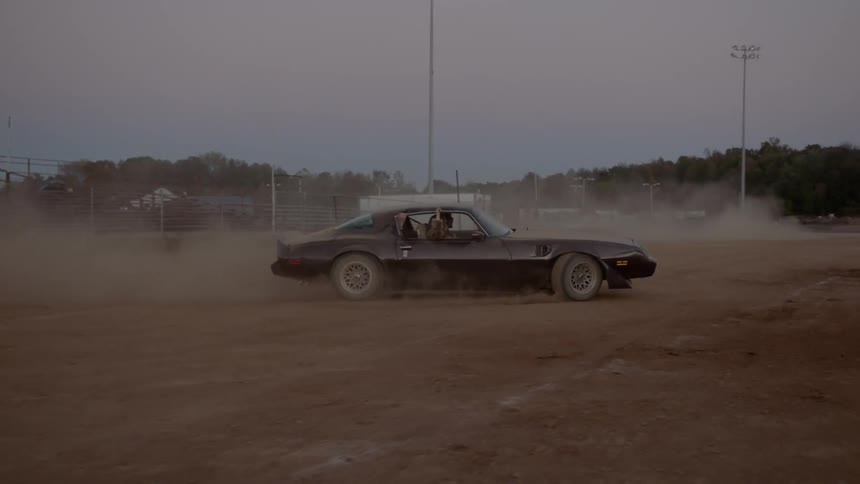 A man and a woman driving a car raising dust