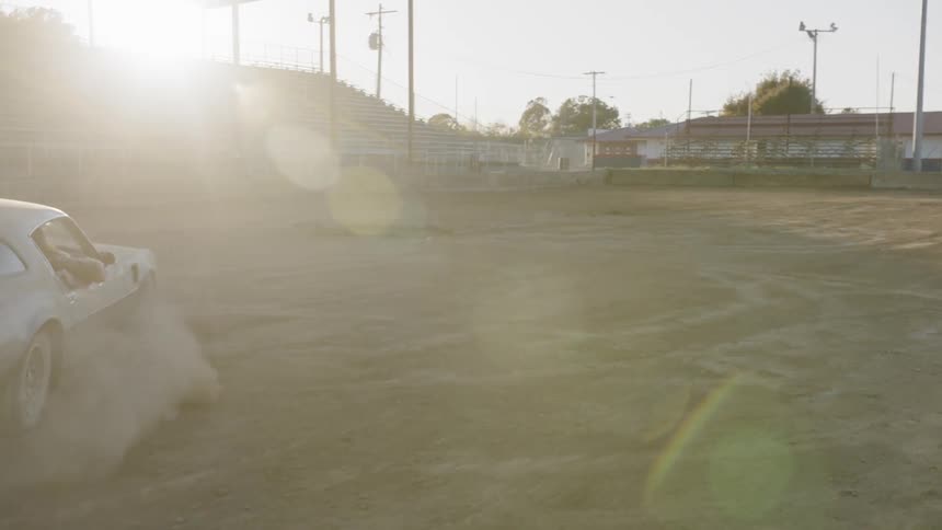 A muscle car makes tight turns on the dirt field of an empty stadium kicking up dust