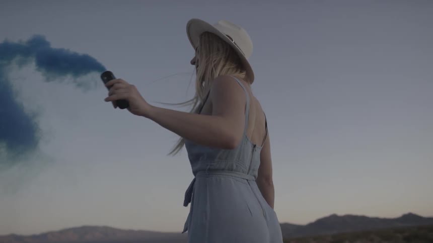 A woman holding a blue smoke stick turns in a circle as the smoke billows around her