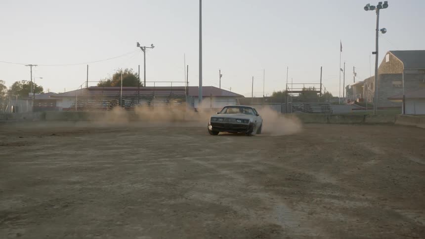 A muscle car kicks up dust in an empty stadium as it makes a turn