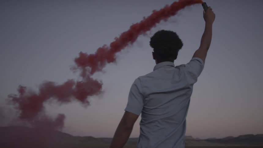 A man holds something pouring out red smoke