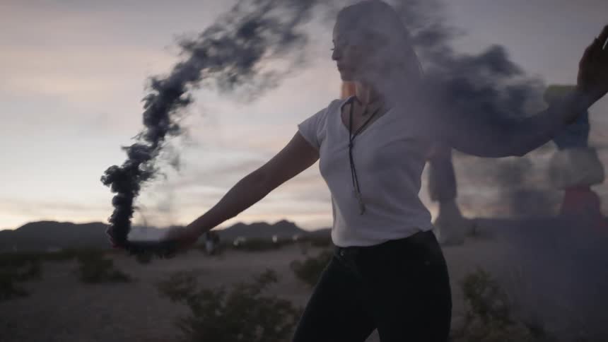 A young woman waves a smoke bomb through the air at sunset