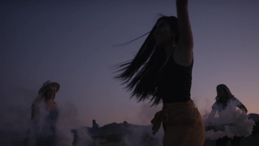 Three women dance while holding flares at sunset