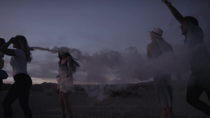 Three young women and a young man playing with smoke flares in the desert
