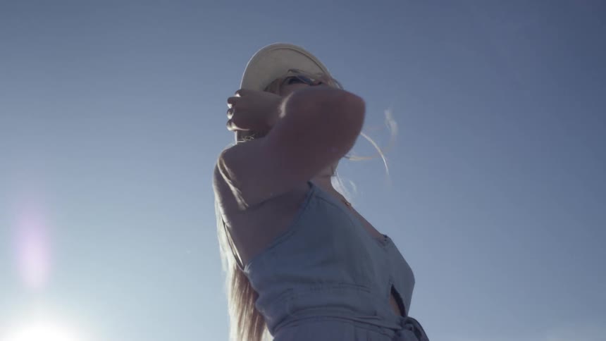 A woman with blonde hair wears a sun hat and looks at installations