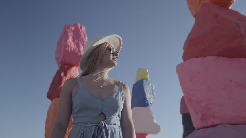 Woman wearing sun hat and sunglasses standing near colored rocks
