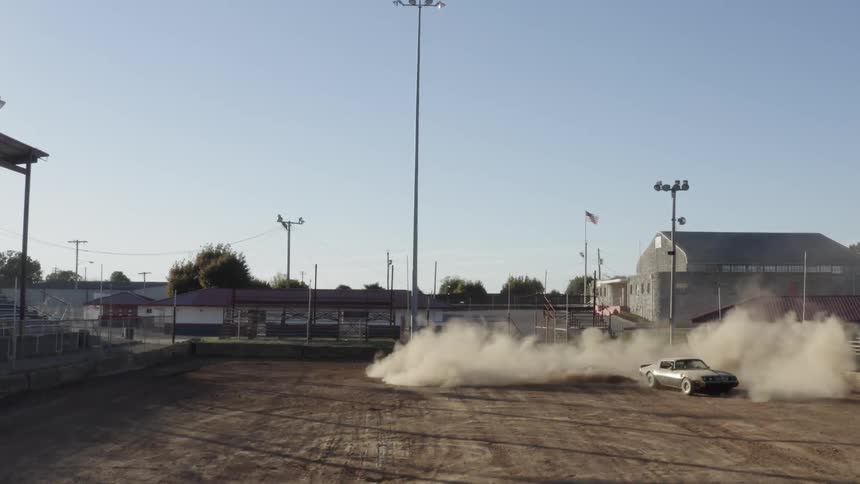 A car drifts and kicks up dust in a dirt arena