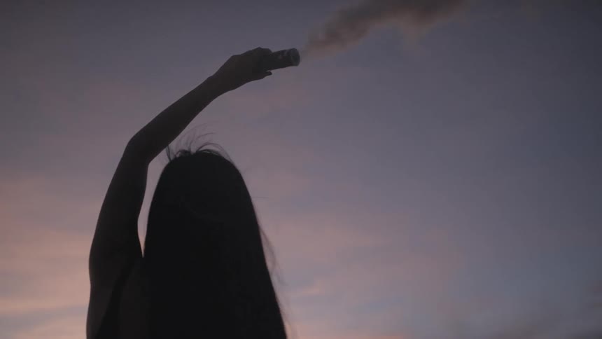 A young woman smiles as she holds a canister above her head that is releasing colored smoke