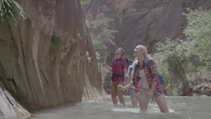 People wade through a river while hiking