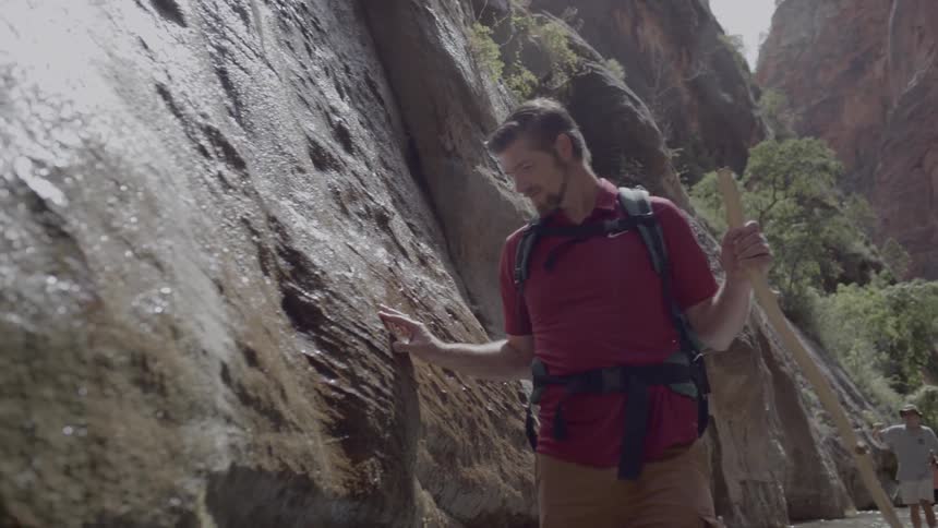 A man walking through a river in the base of a canyon