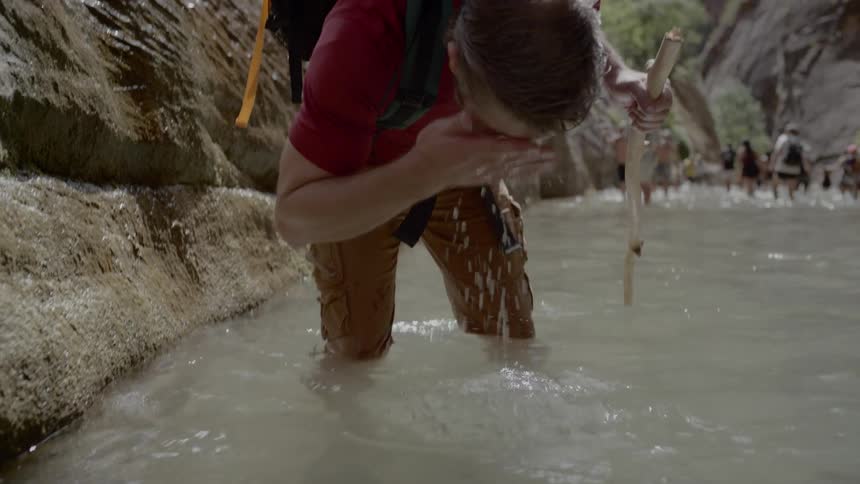 A man hiking in the river in a canyon where he takes water and splashes it on his face