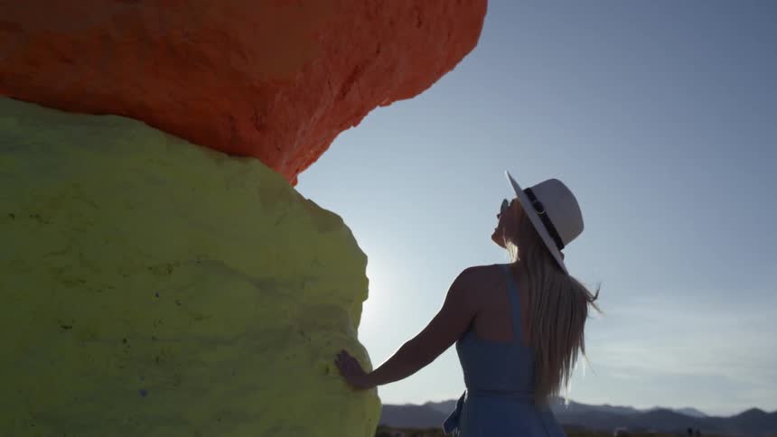 A young woman walks towards a large colorful sculpture and puts her hand on it and looks up at it