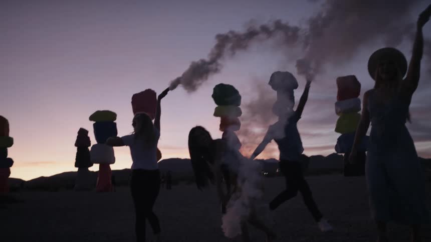 Friends dancing and playing with smoke bombs on desert