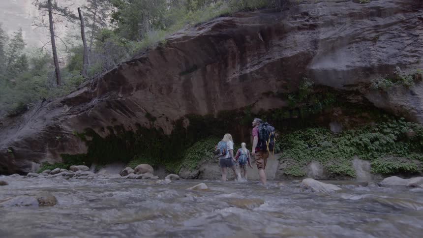 Hikers with backpacks cross a flowing river in the wilderness