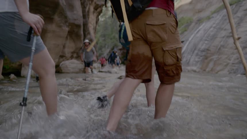 A group of people walk along a stream between two mountains