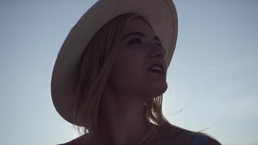 The sun shines behind a blonde woman wearing a hat outside