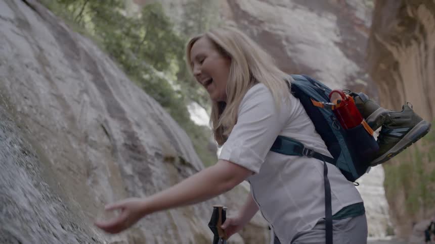 A woman with a backpack taking water from a waterfall and putting it on her face