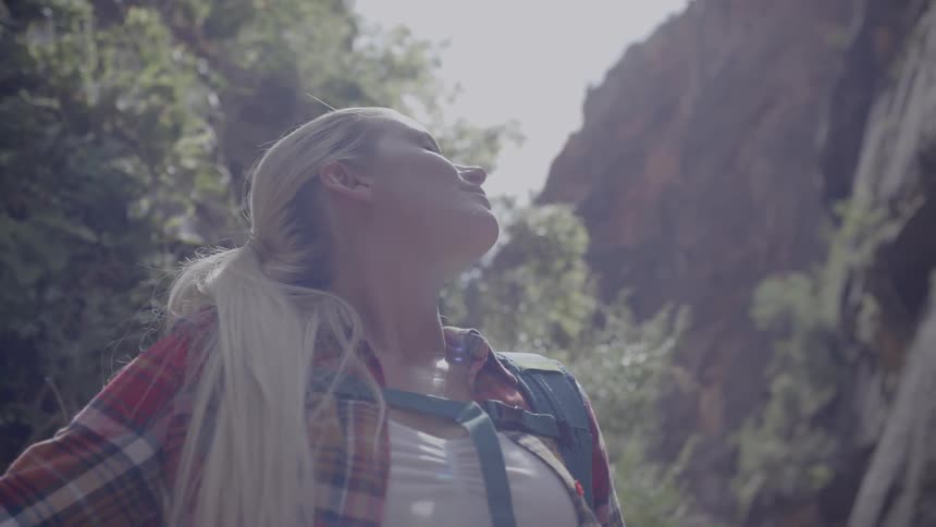 Blonde woman looks up and takes a deep breath on a sunny day in the forest