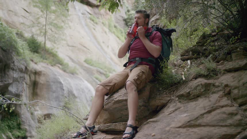 A man sits down on a rock to drink