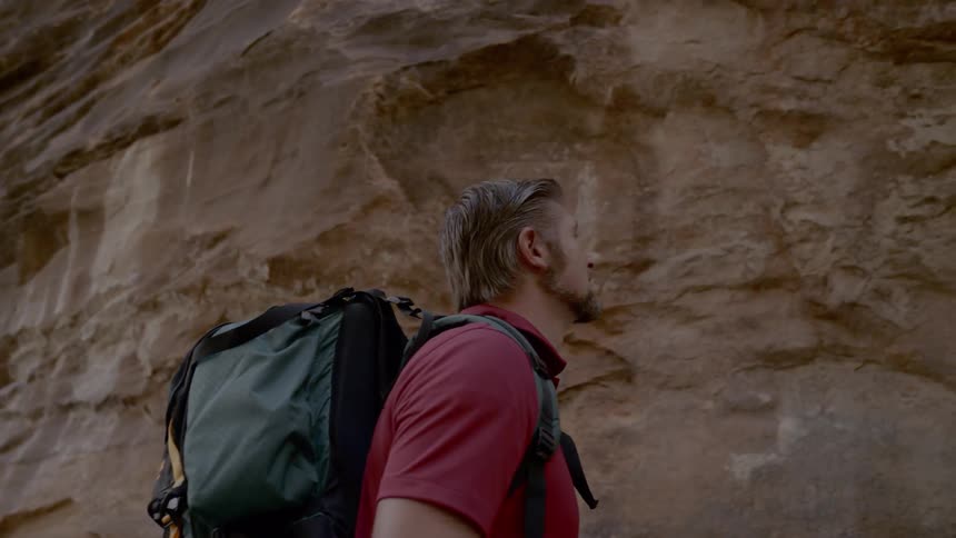 A man with a backpack looks around while hiking in a canyon