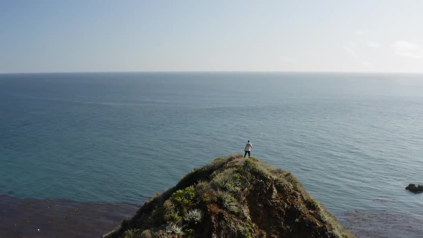 A person standing on top of a cliff looking at the ocean