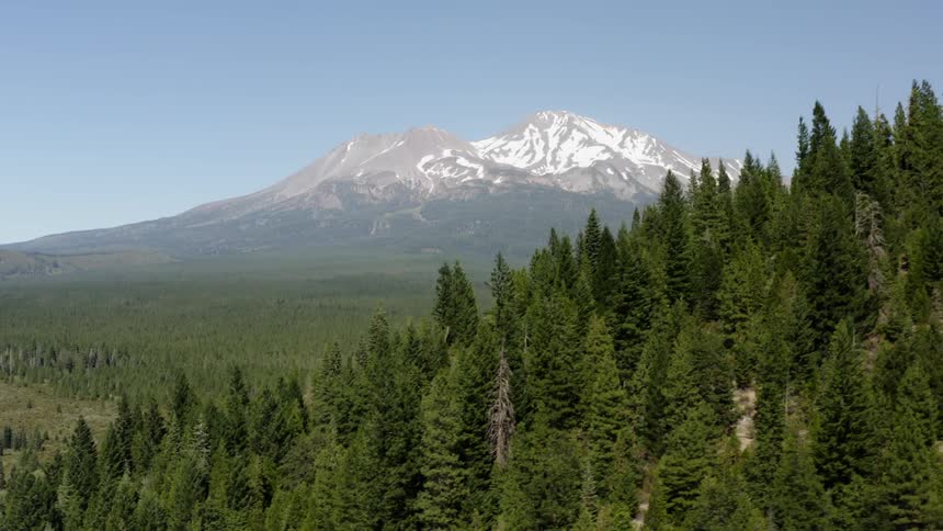 A snow capped mountain in the distance behind a mountain covered in forest