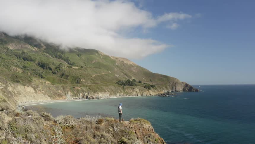 A man stands at the cliff looking toward the ocean