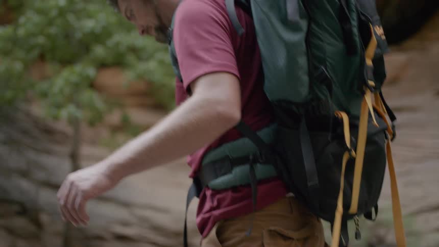 Man with backpack wearing sandals crossing shallow river