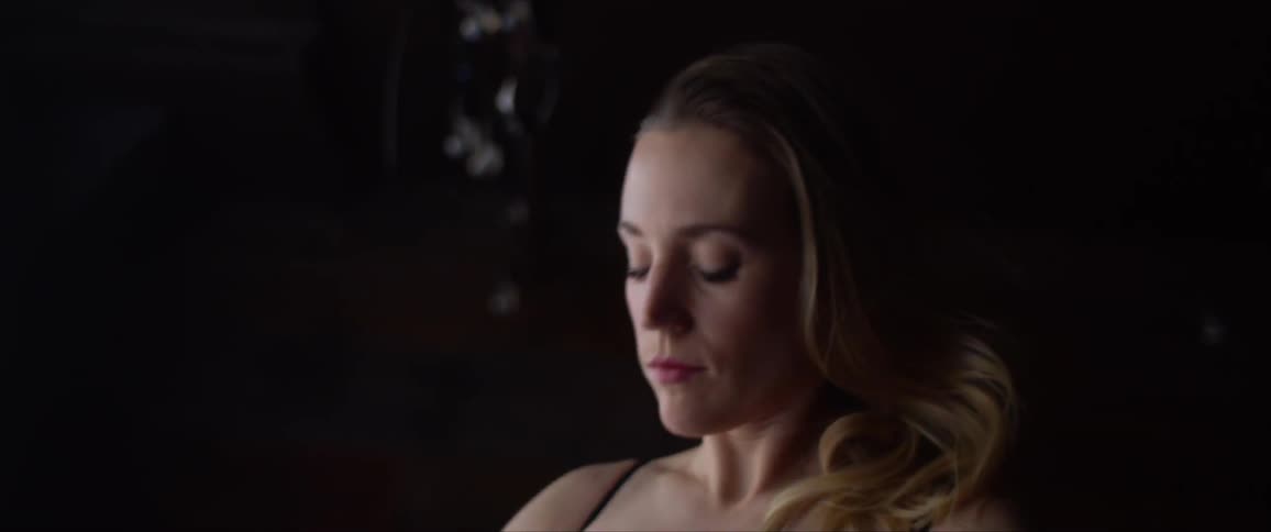 Blonde woman stretches her arms above her head in a dark room