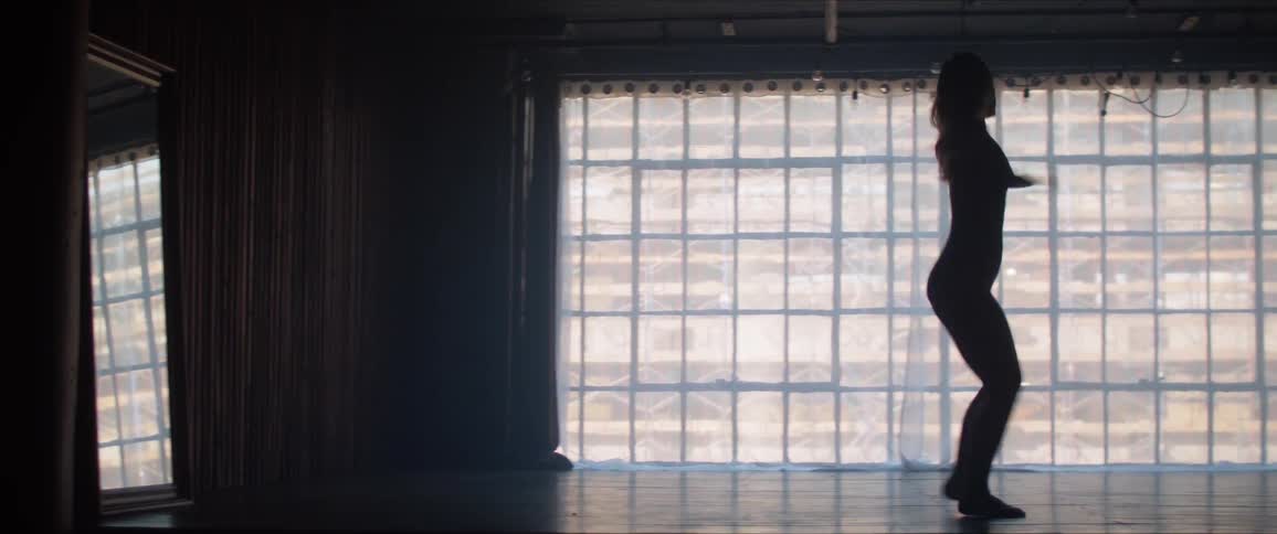 A womans silhouette dances in front of the window in the dark room