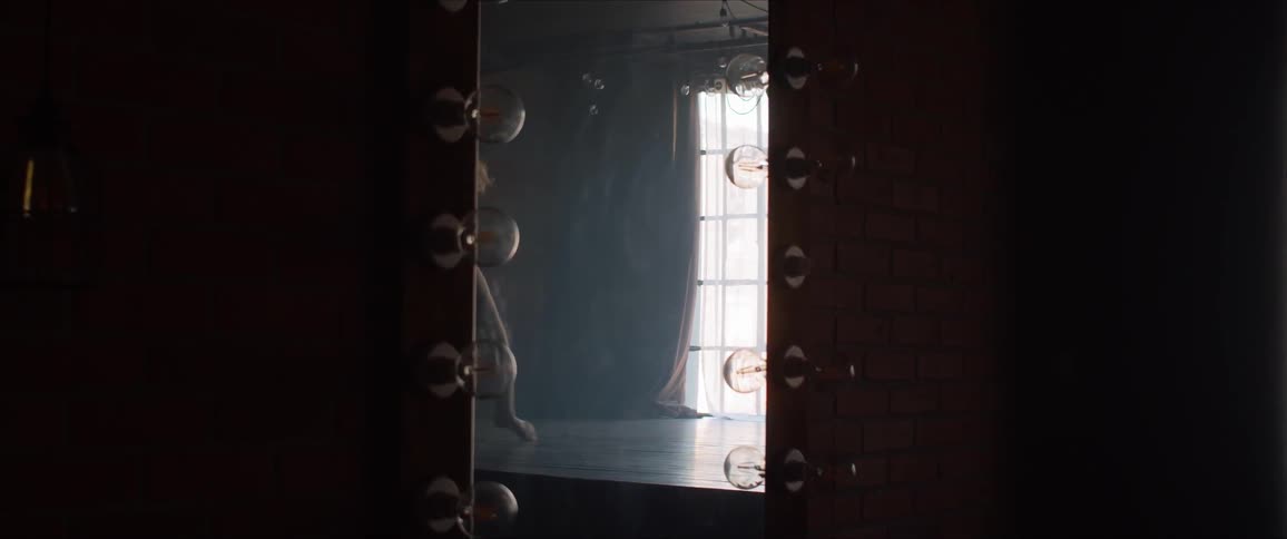 A ballerina silhouette dances in front of the mirror in a dark studio