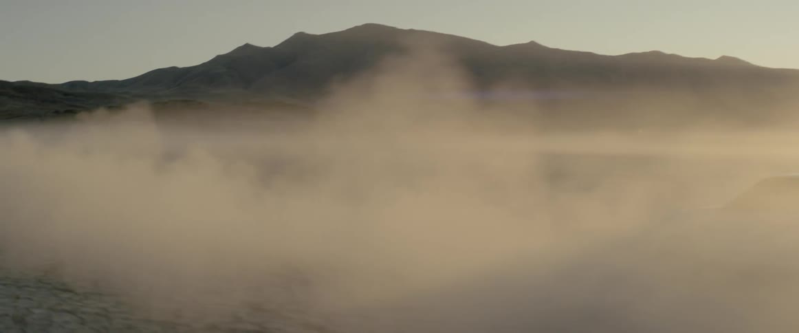 Two suvs kick up dust while speeding through a desert at sunset