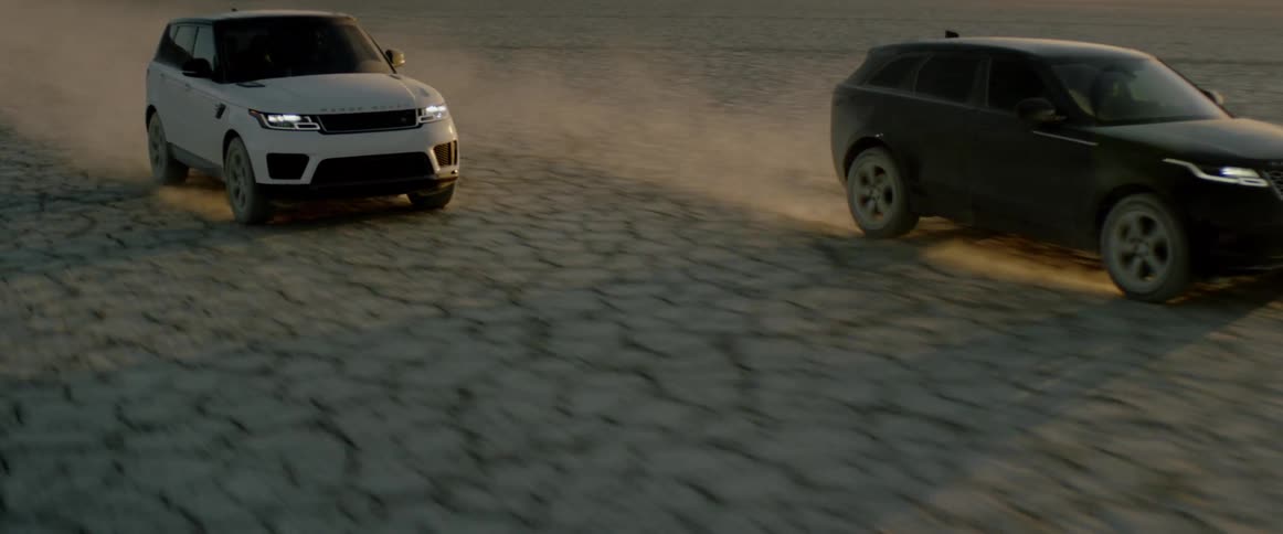 Two cars race across desert with mountains on the horizon
