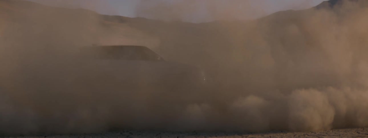 A swirling dust cloud is created by an suv circling another vehicle in the desert