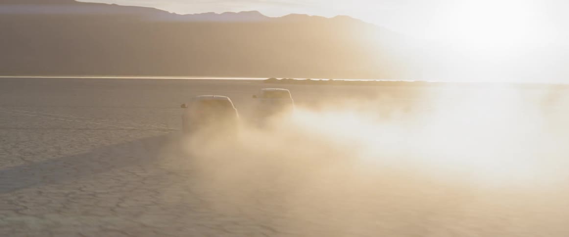 Two suvs drive away across the desert into the sunset