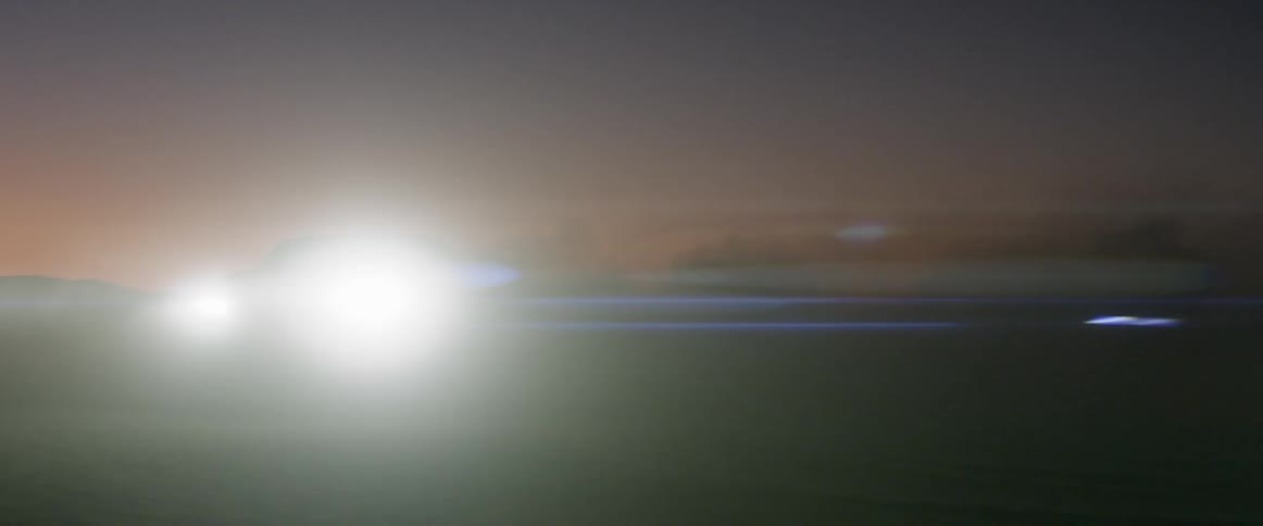 Two cars make a left hand turn with their lights on