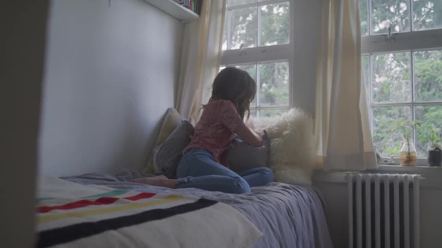 A woman lays in bed leaning on the windowsill